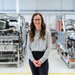 Smiling woman engineer standing confidently in a modern industrial workshop setting.